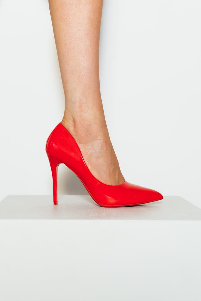 Close-up of a red high heel shoe worn by a woman against a white background.